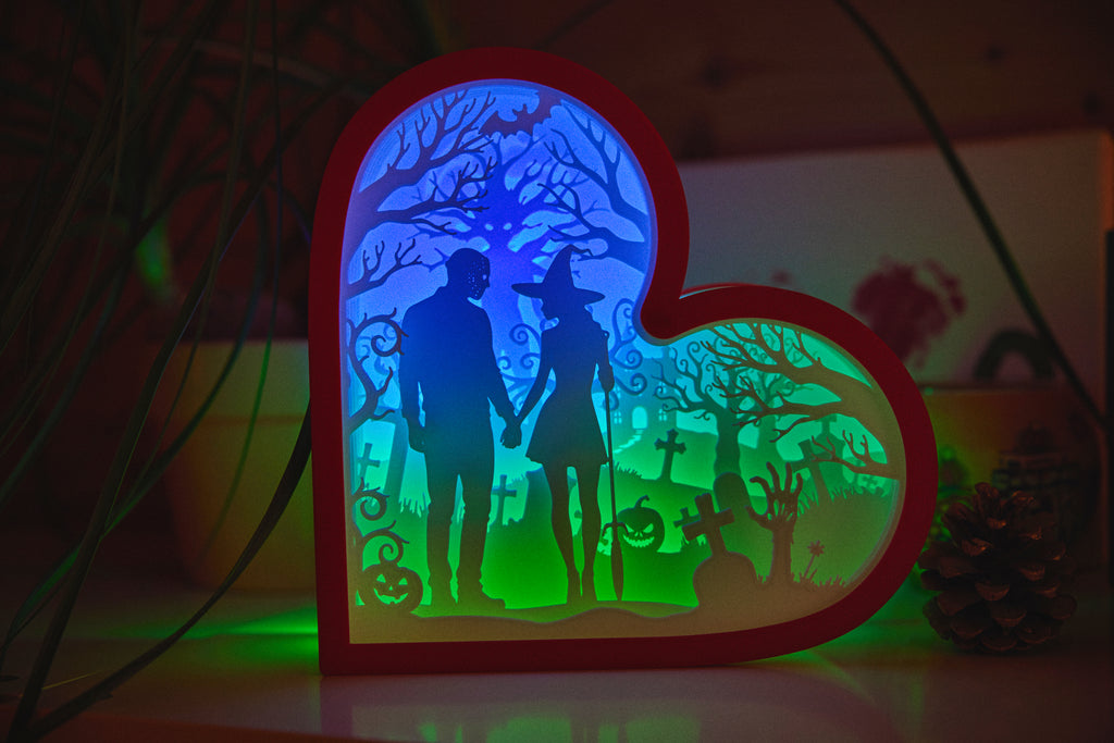 Heart-shaped light box with a silhouette of a couple in a graveyard scene, glowing in the dark.